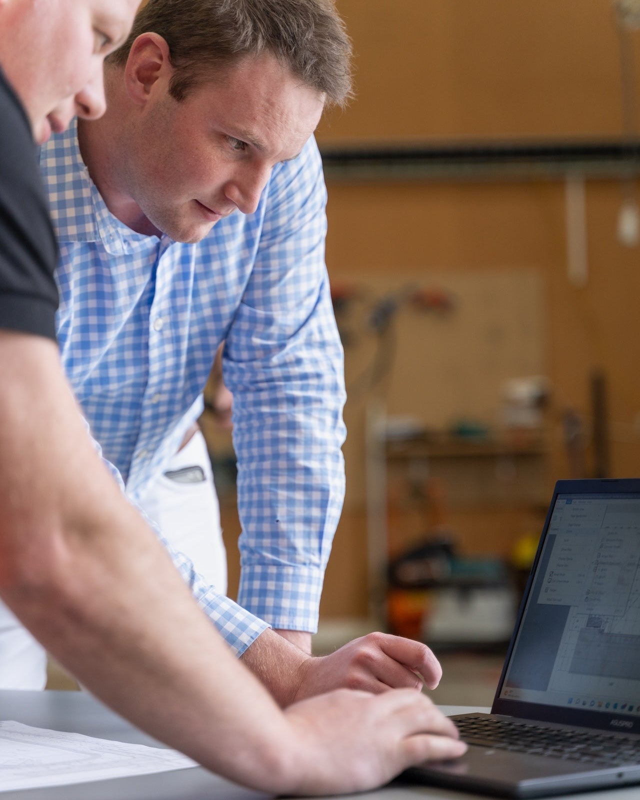 Two men working on a laptop at a table in an indoor setting