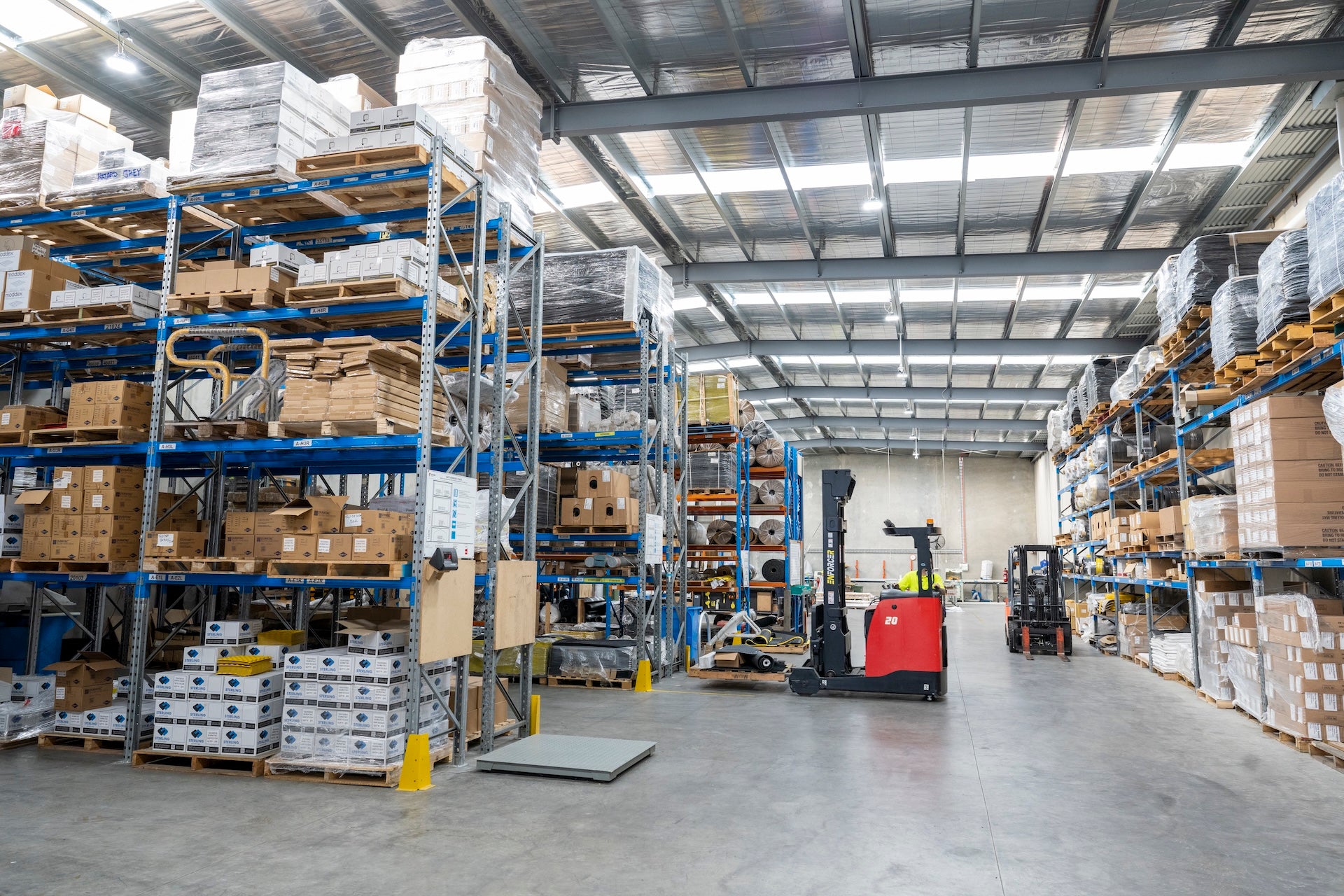 Warehouse interior with shelves stocked with boxes and forklifts.